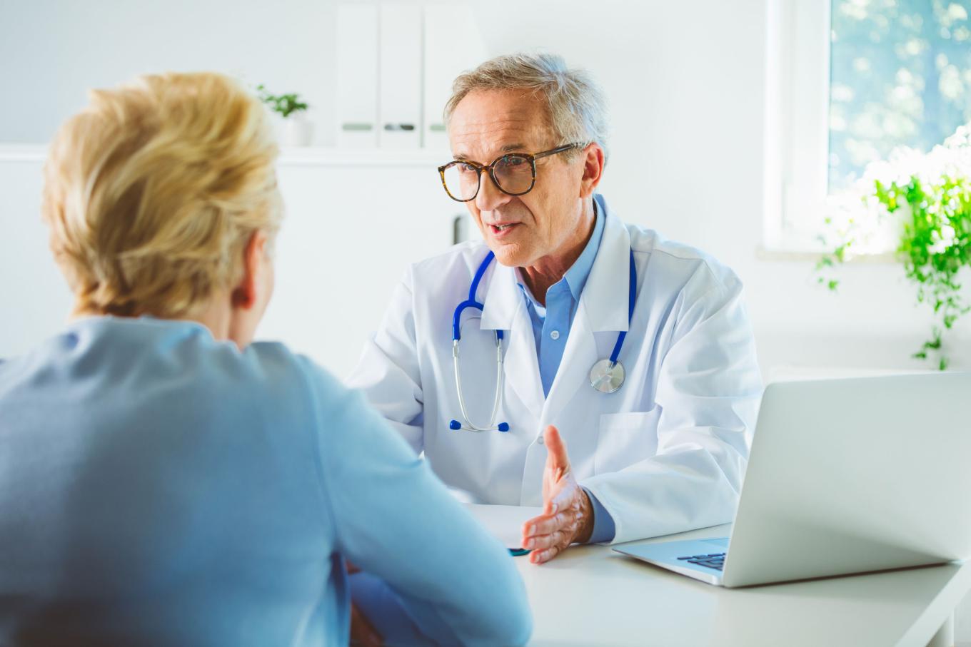 Senior male doctor talking with female patient in hospital room